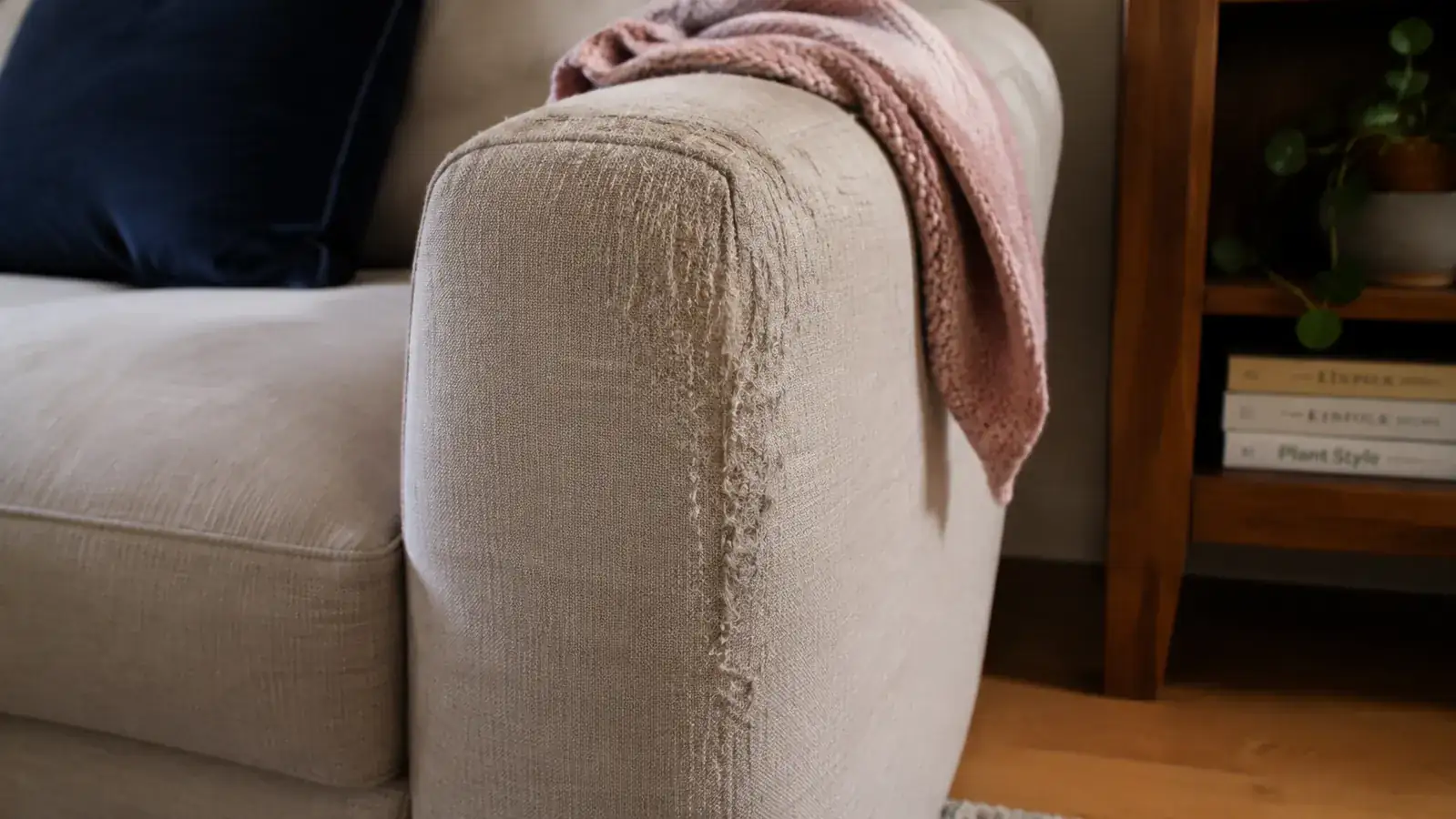 Close-up view of a shredded couch armrest corner showing claw damage from a cat
